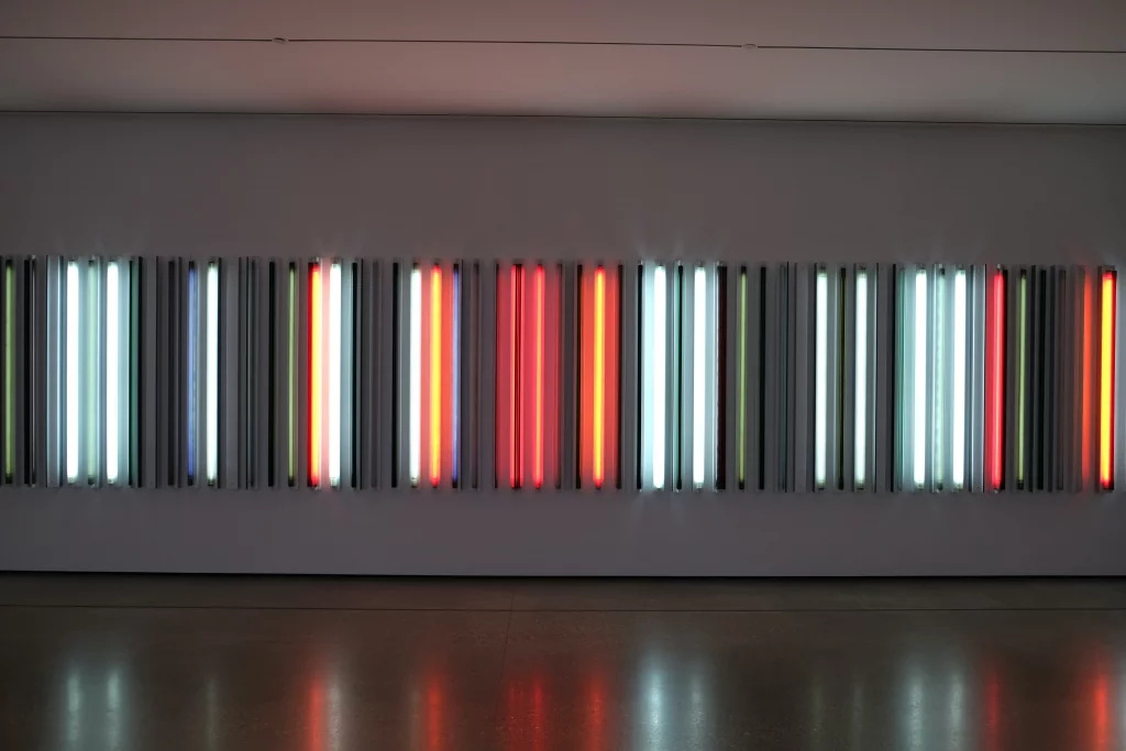 Instalación de arte contemporáneo en galería con hileras de luces de neón, por Mike Von, reflejando estrategias de galería para atraer visitantes con exhibiciones inmersivas e interactivas.
