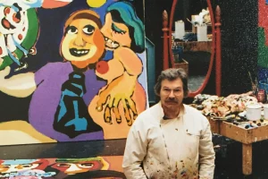 El artista Karel Appel, capturado por Matheus Bertelli, posa frente a una de sus obras coloridas que reflejan la esencia del movimiento artístico CoBrA.