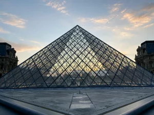 Vista de la Pirámide del Louvre al atardecer con cielo parcialmente nublado, una estructura icónica que atrae a coleccionistas de arte y turistas en París, fotografiada por Radubradu.