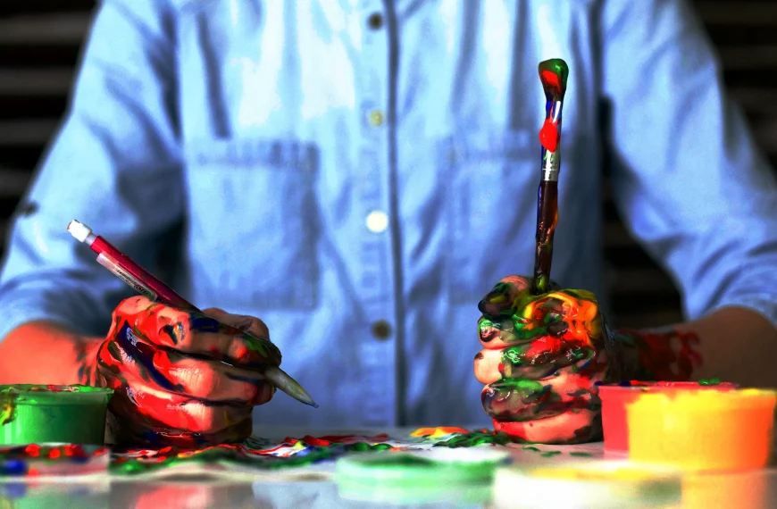 Manos de artista cubiertas de pintura multicolor sosteniendo pinceles, representando el proceso creativo de Alice Dieterich, destacando cómo hacer SEO para artistas a través de la obra visual