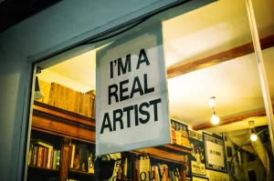 Vista interior del estudio del artista Chris Curry, demostrando cómo hacer SEO para artistas al exhibir de manera visible un cartel que proclama 'I'M A REAL ARTIST', fomentando la identidad y la marca personal en el espacio creativo.